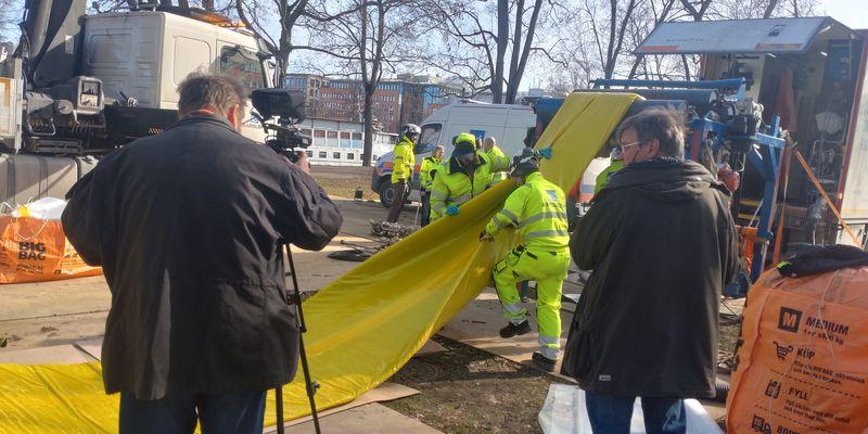 Ove Wennerholm och Michael Baumgarten filmar och fotograferar hur det flexibla fodret förs genom brunnen ner till ledningen. Den gula skyddsplasten på fodret gör att det inte sker en för tidig härdning i solljuset ovan jord. I bakgrunden syns de stora träden längs med Fyrisån som sparas tack vare den schaktfria metoden.